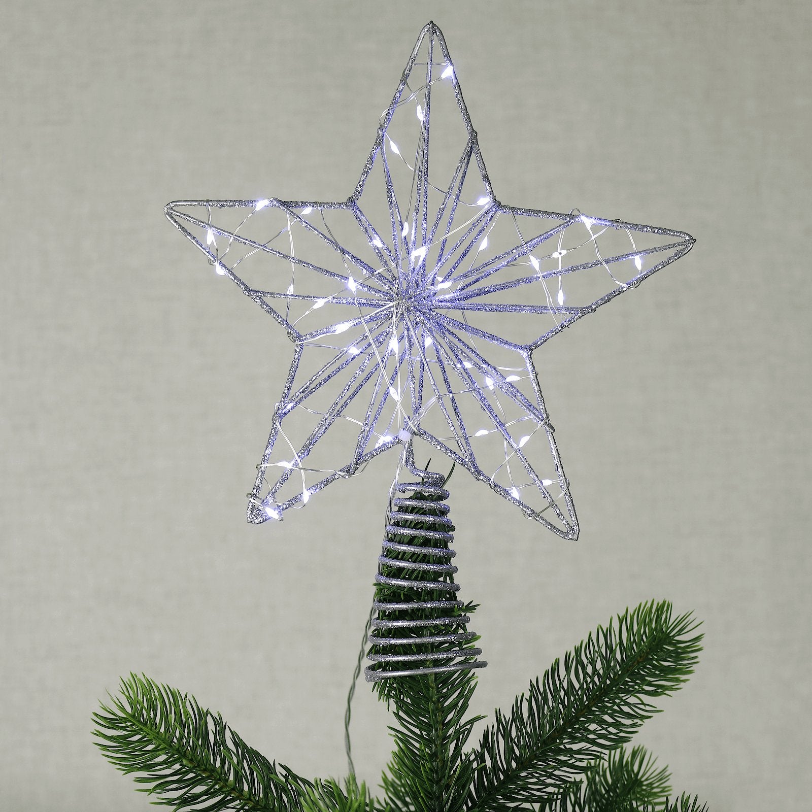 silver glitter finish star tree topper on top of pine christmas tree with bright white LED micro lights